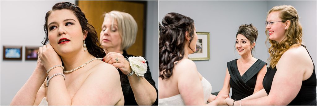 Mother of the groom helping bride put her necklace on; bridesmaids holding bride's hand, all smiling
