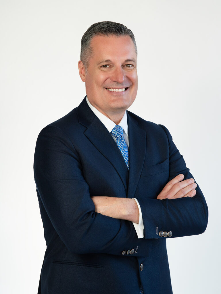 Headshot of Noble McIntyre in a navy blue suit with a white button down and blue/silver checkered tie. He is smiling at the camera.